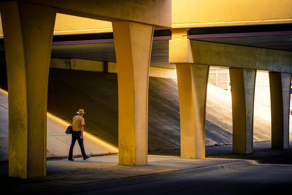 Man in wide-brimmed hat walks through nondescript concrete freeway underpass.